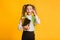 Embarassed Elementary Student Looking At Camera Holding Books On Yellow Background