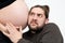 Embarrassed bearded man in casual clothes is listening to his pregnant wife`s tummy, isolated over white background