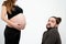 Embarrassed young bearded man looking at the camera while his pregnant whife in black clothes stands near him and holds