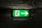 Emergency exit light green sign on brick ceiling in the dark