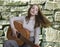 Emotion concept. Portrait of a young girl playing the guitar in front of stone wall