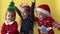 Emotion Cute Happy 3 Friends Baby Girl Boy Putting Hand Together In Santa Suit Looking On Camera At Yellow Background