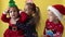 Emotion Cute Happy 3 Siblings Friends Baby Girl And Boy Kissing in Santa Suit Looking On Camera At Yellow Background