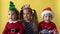 Emotion Cute Happy Cheerful 3 Siblings Friends Baby Girl And Boy in Santa Suit Looking On Camera At Yellow Background