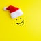 Emotion of a laughing face painted on on a yellow background under a red Santa Claus hat. Concept of happy new year and christmas