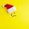 Emotion of a sad crying face painted on a yellow background under the red Santa Claus hat. Concept of not happy new year and