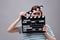 Emotional actress with clapperboard on grey background. Film industry
