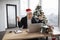 Emotional adult in Santa hat lifting hands while looking at computer screen