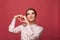 Emotional charming young female smiling and making heart on red background