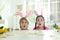 Emotional children wearing bunny ears headbands at table with Easter eggs