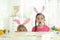 Emotional children wearing bunny ears headbands at table with Easter eggs