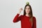Emotional clueless young female with long hair dressed in red sweater with green apple on head having dissatisfied