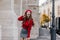 Emotional female model in soft red sweater posing in front of old white building. Portrait of graceful european girl