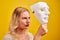 Emotional female person with white mask on yellow background. Internet fraud concept, anonymous, incognito, bipolar personality di