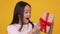Emotional happy asian girl enjoying gift, looking at box with excitement, orange studio background, slow motion