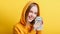 Emotional happy teenage blonde girl in hood win money cash holding dollars isolated on color yellow background. Portrait