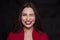 Emotional head shot portrait of a brunette caucasian woman in red dress and with red lips on black background. She winked