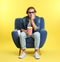 Emotional man with 3D glasses, popcorn and beverage sitting in armchair during cinema show