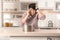 Emotional man calling plumber near table with saucepan under leaking water from ceiling