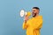 Emotional middle eastern man shouting with megaphone, making announcement or sharing news, blue background