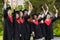 Emotional multiethnic students in graduation costumes raising diplomas