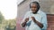 Emotional senior African American man listening music in headphones enjoying song audio player app on building