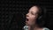 Emotional singing. Beautiful caucasian woman singing in recording studio. Vocal music studio with microphone and black background.
