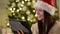 Emotional Woman in Santa Hat Using Gadget During the Celebration of Xmas. Amazing Brunette with Long Hair and Charming