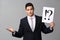 Emotional young businessman holding paper sheet with interrogation and exclamation marks on grey background