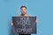 Emotional young man holding sign with phrase Your Silence Is Complicit on light blue background. End racism