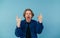 Emotional young man rocker in shirt showing hands gesture of heavy metal and shouting, looking at camera, isolated on blue