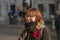 An emotional young woman of 20-25 years old with glasses, dyed red hair and a little overweight against the background of the city