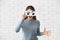 Emotional young woman hiding face behind sheet of paper with drawn eyes against white brick wall