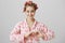 Emotive charming european woman in hair-curlers and pyjamas, looking feminine and showing heart gesture over chest