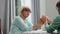 Empathic senior blond woman in eyeglasses holding hands with friend and talking. Portrait of confident Caucasian retiree