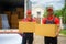 The employees of the House Removals company are standing behind the truck with boxes and smiling