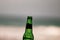 Empty 33cl bottle of beer close up, edited; sea view background. iconic image