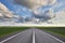 Empty asphalt highway outside the city among green fields and against a beautiful cloudy sky