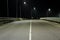 An empty asphalt road with bumpers and a solid white line lit by streetlights