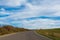 Empty asphalt road, dried vegetation, blue sky