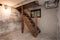 Empty basement in abandoned old industrial building with little light and a wooden stairs