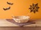 Empty basket with tablecloth on wooden table over orange wall and paper decorations background. Halloween mock up for design and