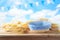 Empty basket with wheat and tablecloth on wooden table over beautiful sky background. Shavuot holiday mock up for design