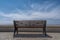 An empty bench against the background of blue sky and clouds in the Park stands on gray paving stones, in front of the parapet