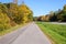 Empty bicycle lane running alongside a road through a colourful forest on a clear autumn day