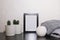 An empty black frame, cacti and succulents in pots, a candle holder and a gray sweater on a table against a white wall