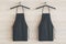 Empty black kitchen aprons on hangers. Light wood background. Chef and cooking concept. 3D Rendering