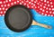 empty black round nonstick frying pan with handle on blue wooden background with red napkin