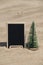 Empty blackboard frame board with copy space for your text or design displays on sandy beach. Christmas tree New Year