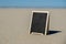 Empty blackboard frame board with copy space for your text or design displays on sandy beach. Summer vacation and